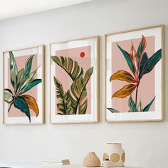 three framed art prints on the wall above a table with vases and plant items