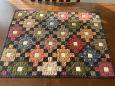 a quilted table runner on top of a wooden table with a chair in the background