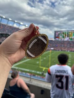 a hand holding a football keychain in front of a stadium filled with people