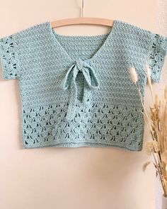 a blue crocheted top with a bow on the front and back, hanging from a wooden hanger