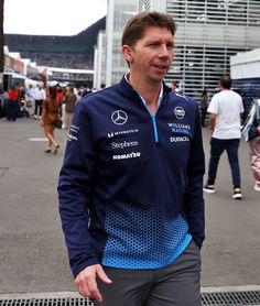 a man standing in front of a building wearing a blue and black jacket with the mercedes logo on it