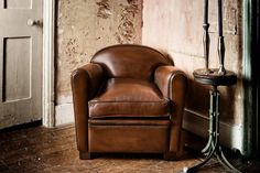 a brown leather chair sitting in front of a lamp next to a wall with peeling paint on it