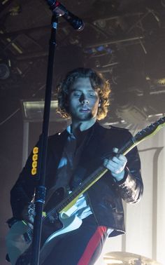 a man with long hair holding a guitar in his right hand while standing on stage