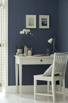 a white desk and chair in front of a blue wall with pictures on the walls