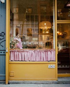 the front window of a flower shop with pink curtains