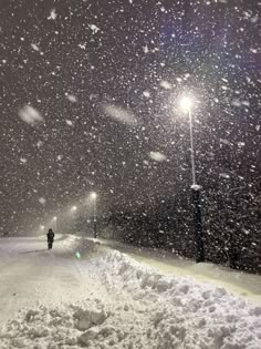 a person walking down a snow covered road at night with street lights in the background