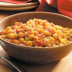 a brown bowl filled with food on top of a wooden table next to silverware