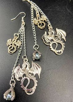 Unique and unusual dragon charm earrings. Adorned with gothic dragon charms and a glass pearl in a dragons talons. There are lightweight earrings which are nickel free and silver plated. They are about 4 inches long. These make a great gift idea! Gothic Metal Jewelry With Dragon Design, Silver Dangle Fantasy Earrings, Fantasy Dangle Earrings For Halloween, Punk Metal Jewelry For Fantasy Events, Halloween Fantasy Dangle Earrings, Fantasy Halloween Dangle Earrings, Handmade Metal Fantasy Earrings, Nickel-free Fantasy Drop Earrings, Handmade Fantasy Metal Earrings