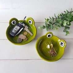 two green frog shaped dishes with keys and money in the bottom one is holding a car key