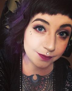 a close up of a person with purple hair and piercings on her nose, wearing a black shirt