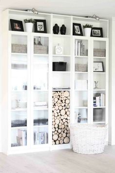 a living room with white bookcases filled with books and baskets on top of them