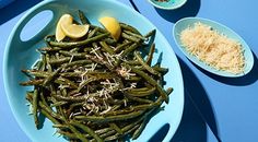 green beans with lemon wedges and parmesan cheese on a blue table top