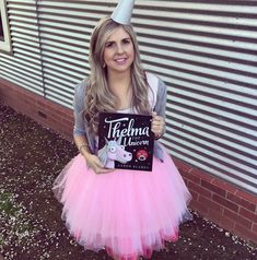 a woman in a pink tutu skirt holding up a sign that says thermo unicorn