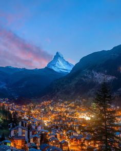 a city at night with mountains in the background and lit up buildings on either side