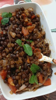 a white bowl filled with beans and vegetables on top of a table next to a fork