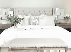 a white bed topped with lots of pillows next to two nightstands filled with flowers