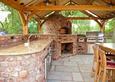 an outdoor kitchen with stone counters and brick oven in the center, surrounded by wood beams