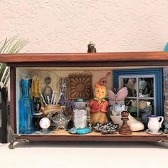 a display case filled with lots of different items on top of a white table next to a potted plant