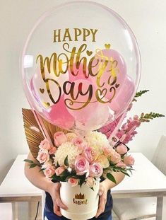 a woman holding a vase filled with flowers and balloons in front of a white table