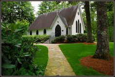 a white church surrounded by lush green trees and shrubbery with a stone pathway leading to the front door