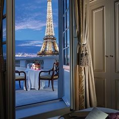 the eiffel tower is seen through an open window in this room with a table and chairs