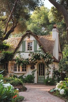 a white house with green shutters and flowers on the front door is surrounded by greenery