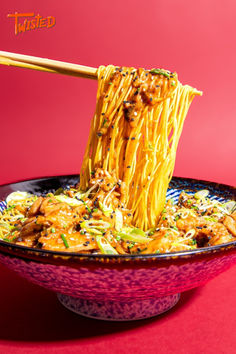 noodles being lifted from a bowl with chopsticks over it on a red surface