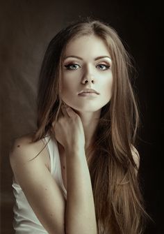 a woman with long brown hair and blue eyes posing for a photo in front of a black background