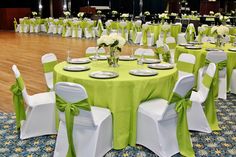 a banquet hall with tables and chairs covered in green cloths, white sashes and flowers