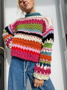 a woman wearing a multicolored sweater and jeans standing in front of a door