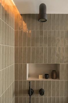 a bathroom with tiled walls and shelving in the corner, along with two black faucets