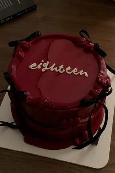 a red cake with writing on it sitting on a white plate next to a book