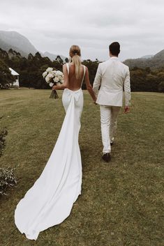 a bride and groom walking in the grass