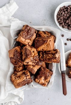 chocolate chip brownies in white bowls next to spoons and napkin on grey surface