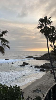 the beach is lined with palm trees as the sun sets over the ocean and rocks