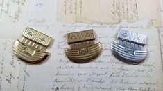 three gold, silver and black pins sitting on top of an old piece of paper