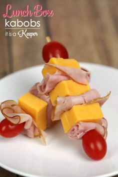 a white plate topped with ham and cheese on skewers next to cherry tomatoes