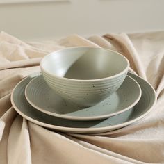 two plates and a bowl on a bed with a beige blanket in the back ground