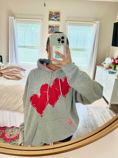 a person taking a selfie in a mirror with a heart sweatshirt on and a phone up to their face