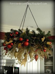 a chandelier hanging from the ceiling decorated with red and gold christmas balls, pineconis, holly berries and golden ribbons