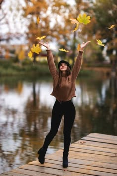 a woman is standing on a dock with her arms in the air and falling leaves