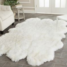 a large white sheepskin rug is on the floor next to a chair and table