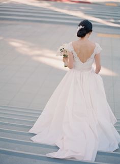 a woman in a wedding dress is walking down the street with her back to the camera