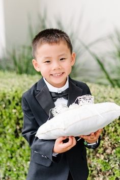 a young boy in a tuxedo holding a pillow