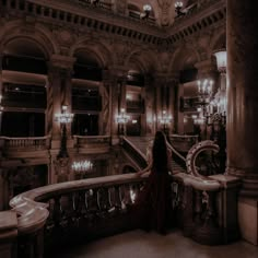 a woman in a long red dress standing at the top of a staircase with chandeliers