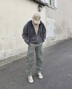 a man standing in front of a building wearing a baseball cap and khaki pants