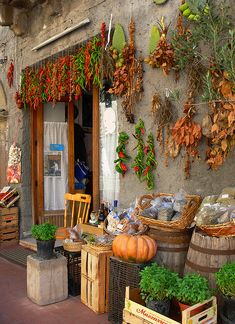 an outdoor market with lots of vegetables and fruits hanging on the building's side