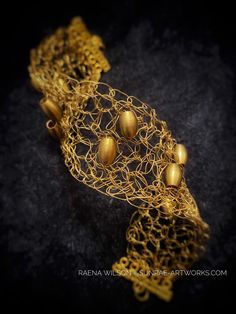 an intricate gold bracelet with five golden balls on it's side, sitting on a black surface