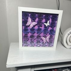 a white frame sitting on top of a table next to a wall mounted butterfly and flowers