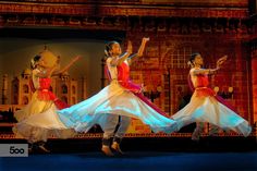 three women in colorful dresses are dancing on stage